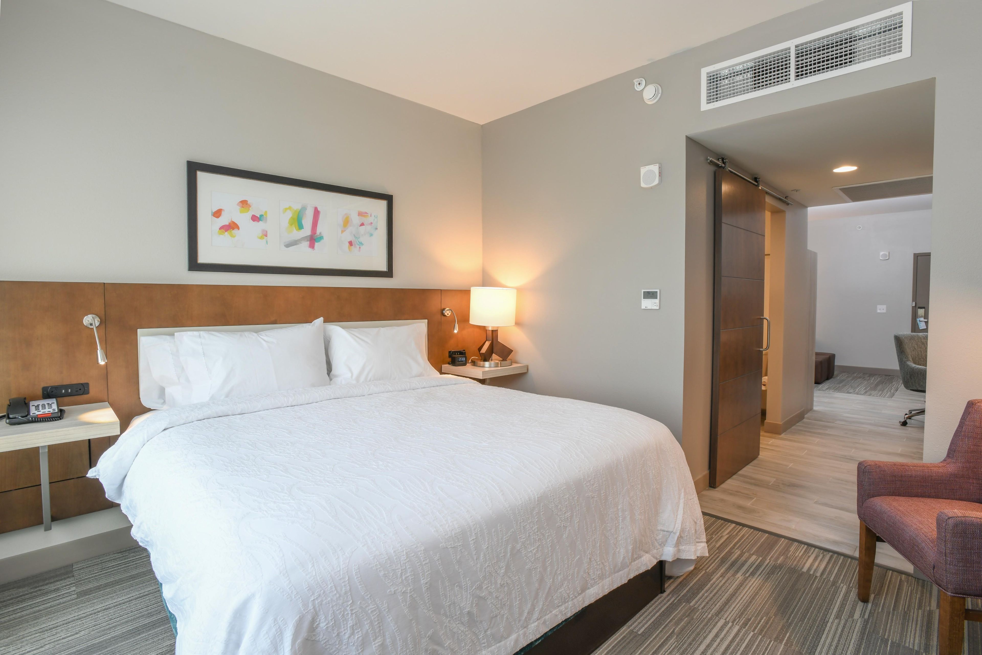 Una habitación de hotel con una cama grande, mesitas de noche, una lámpara, un reloj y un cuadro en la pared.
