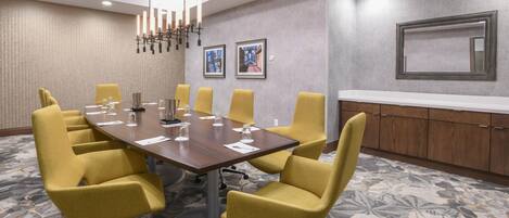 A conference room with a large table, yellow chairs, a white counter, and framed pictures on the wall.