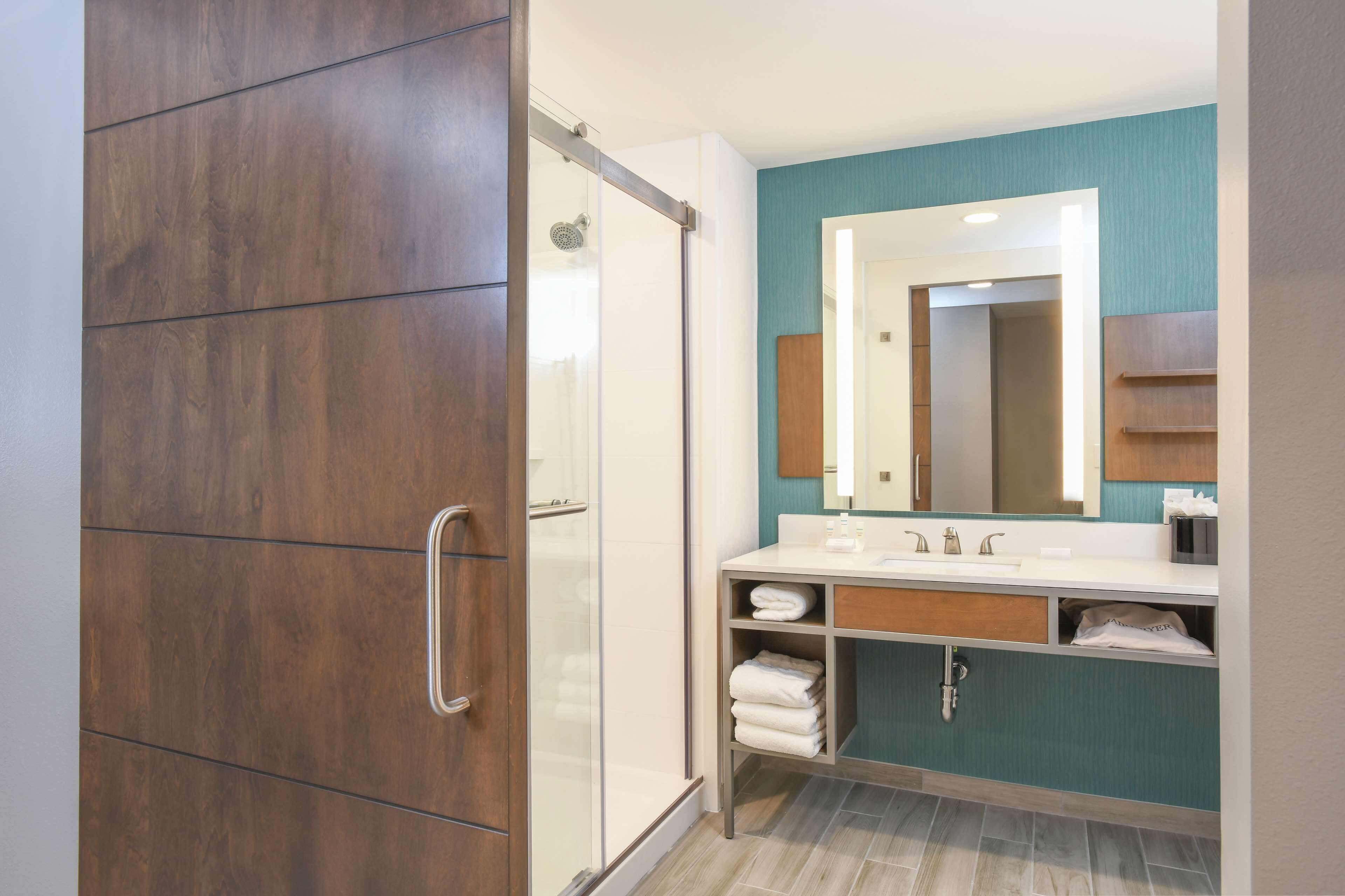 A modern bathroom with a wooden wardrobe, a glass shower enclosure, and a vanity with a mirror and towel rack.