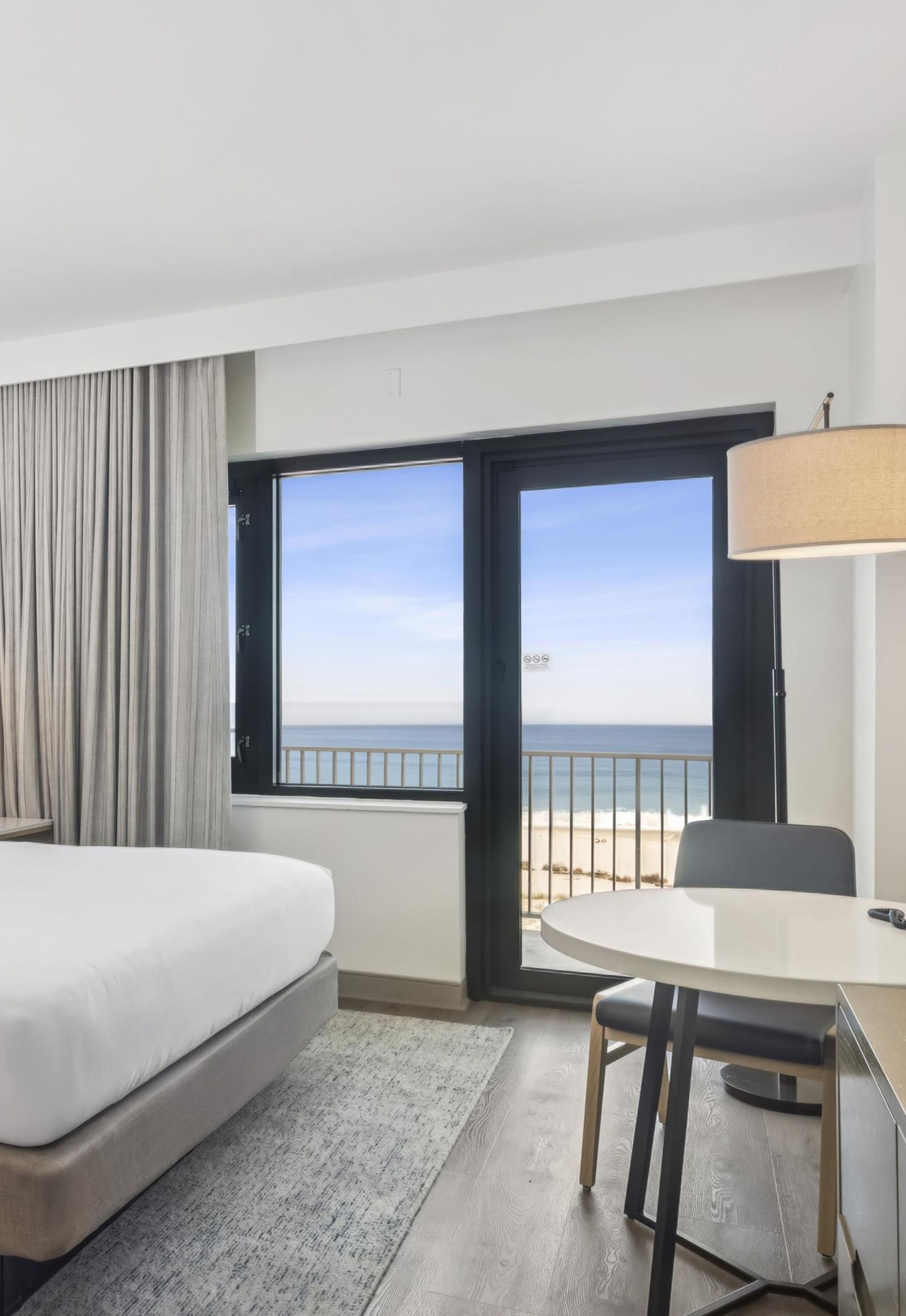 A hotel room with a bed, a dining table, and a view of the ocean.