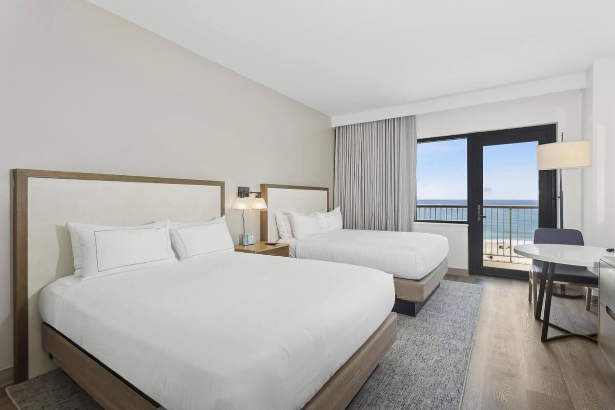 Habitació d'hotel amb dos llits, una taula de treball i un balcó que fa a la mar.
