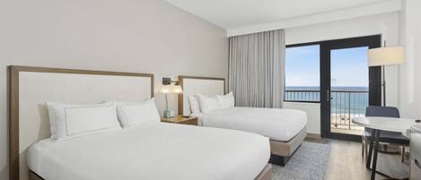 A hotel room with two beds, a desk, and a balcony with a view of the sea.