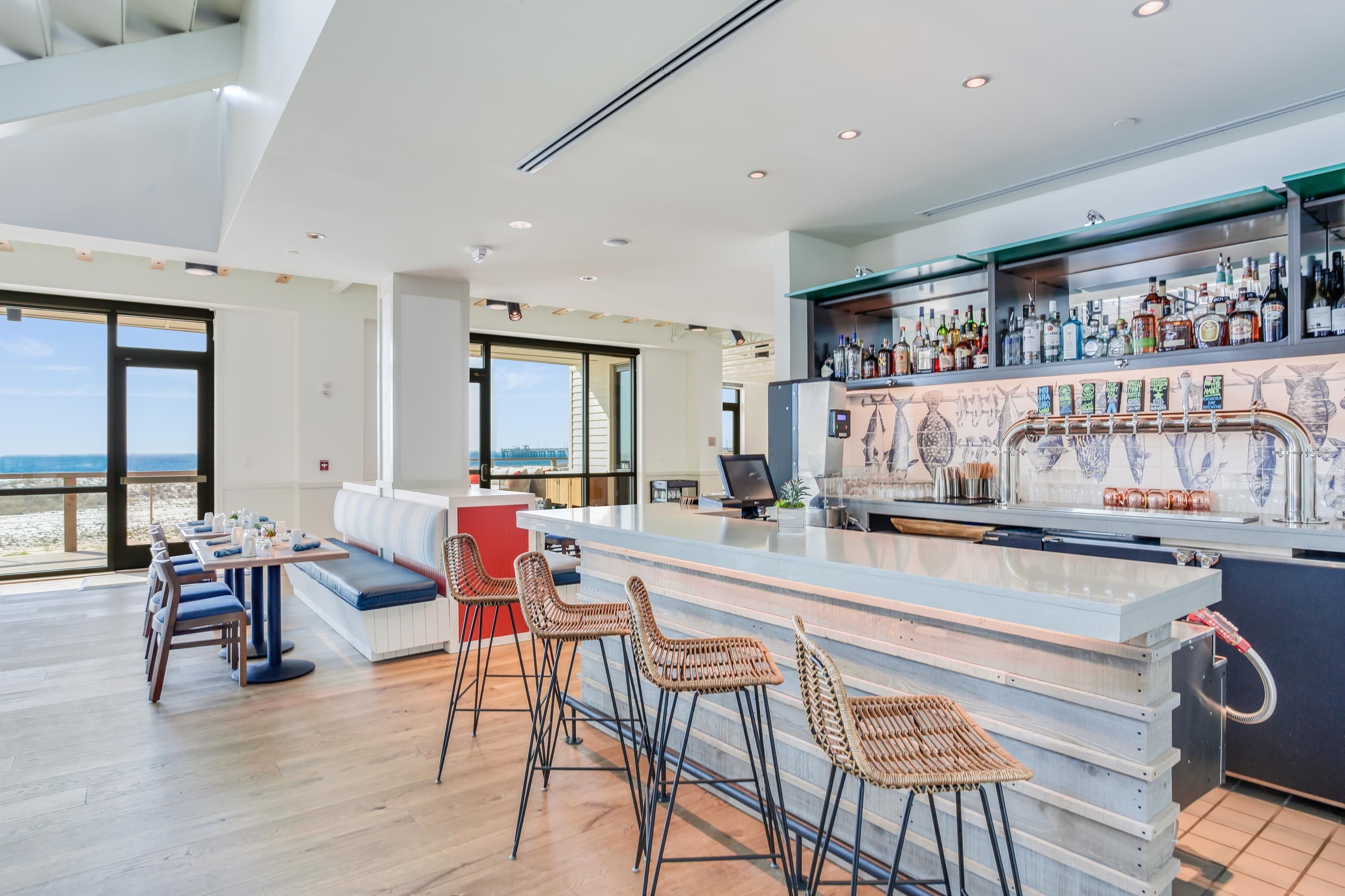 A modern bar area with a long counter, bar stools, and a seating area with a view of the beach.