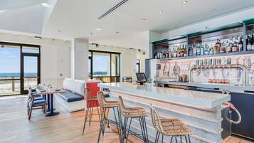 A modern bar area with a long counter, bar stools, and a seating area with a view of the beach.