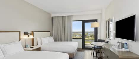 A hotel room with two beds, a TV, a desk, and a view of the outdoors.