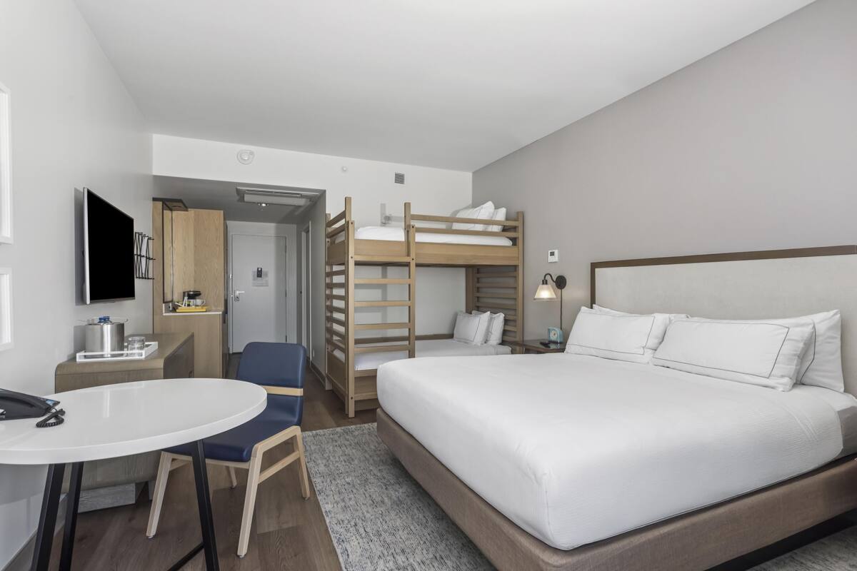 Habitació d'hotel amb una llitera, un escriptori amb una cadira, un televisor de pantalla plana i una petita cuineta.