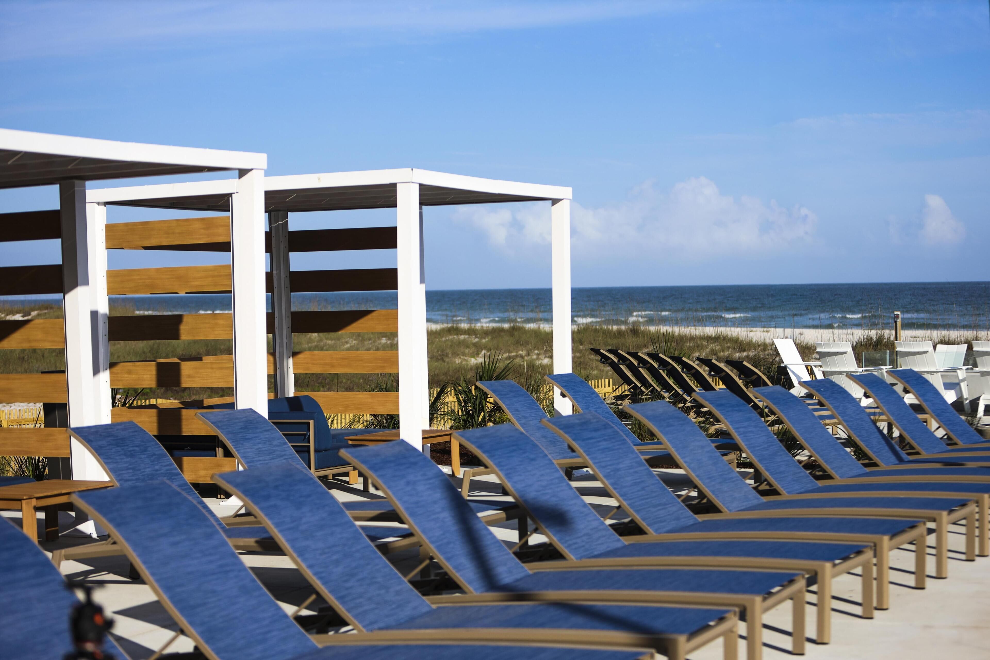 A beachside lounge area with rows of sun loungers and wooden structures, overlooking the ocean.