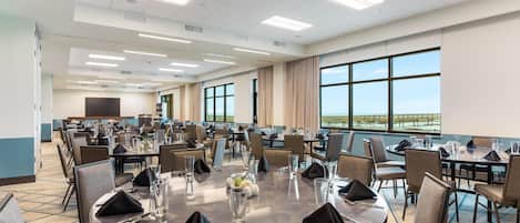 Un salón de conferencias con mesas redondas, sillas y un ventanal con vistas.
