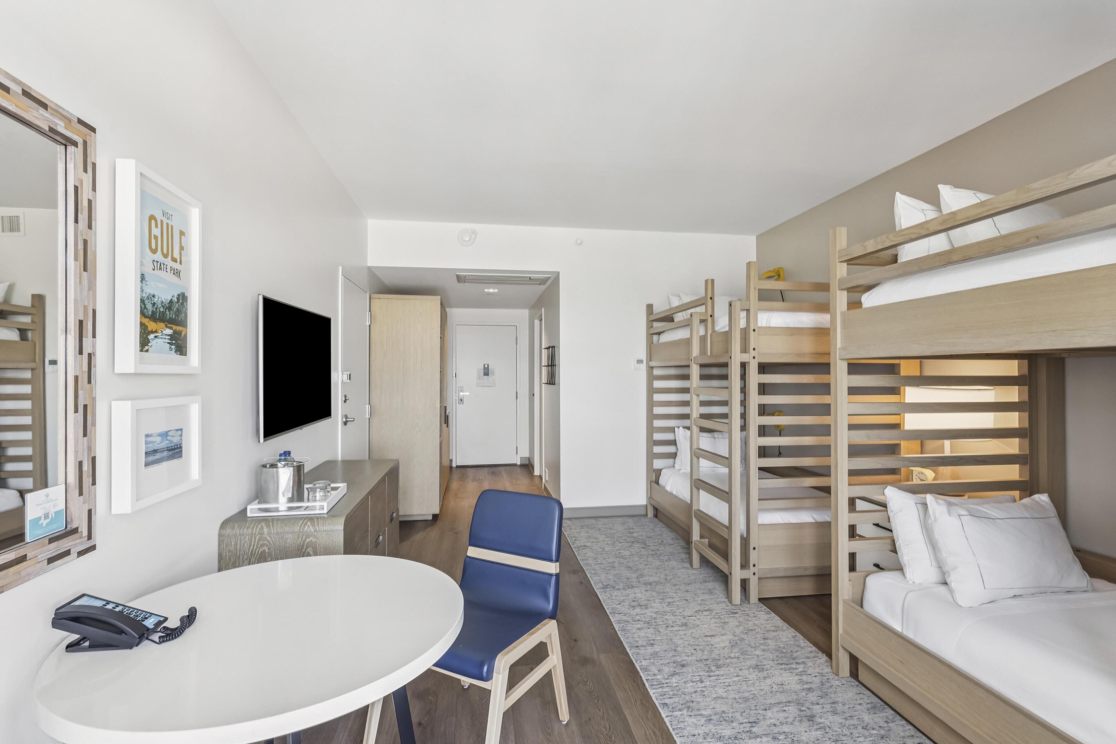 Habitación de hotel con literas, un escritorio con teléfono, televisión y cuadros en la pared.