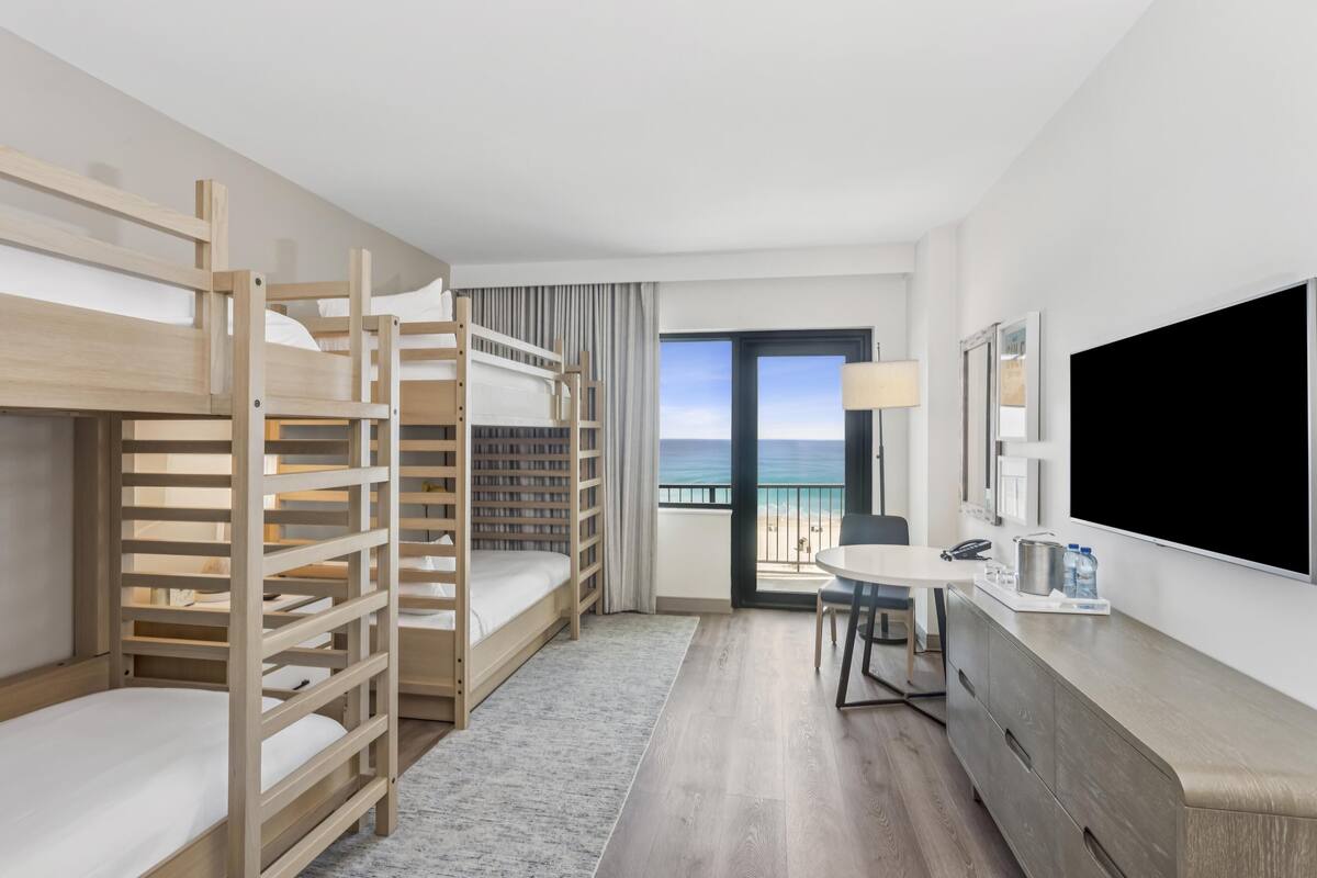 Habitació d'hotel amb llits superposats, un escriptori, una televisió i vista a la platja.