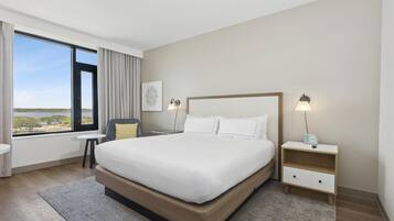 A modern hotel room with a large bed, a bedside table with a lamp, a small side table, and a view of the outdoors.