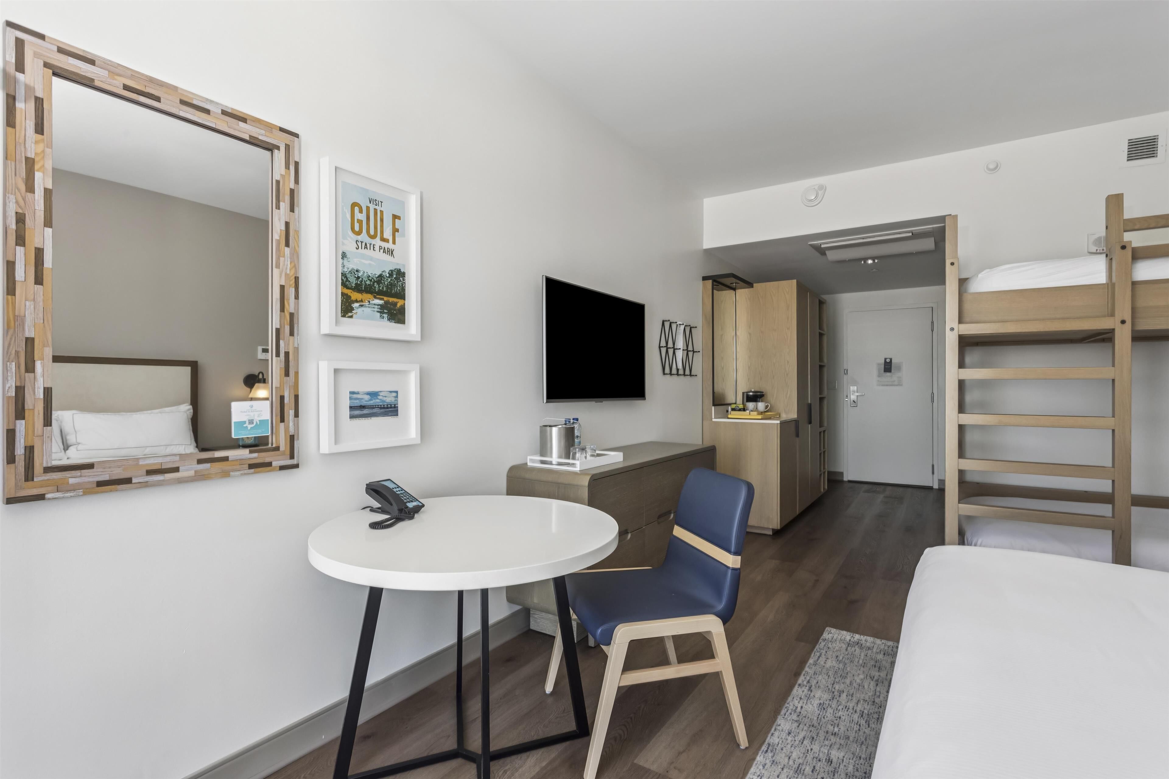 Une chambre d’hôtel comprenant un lit, un bureau avec une chaise, une télévision, un miroir et un lit superposé.