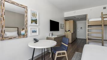 Ein Hotelzimmer mit einem Bett, einem Schreibtisch mit Stuhl, einem Fernseher, einem Spiegel und einem Etagenbett.