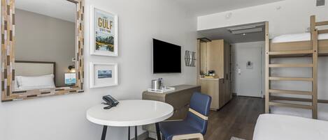 A hotel room with a bed, a desk with a chair, a television, a mirror, and a bunk bed.