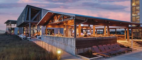 A modern building with a covered outdoor seating area, a bar, and a staircase leading to an upper level.
