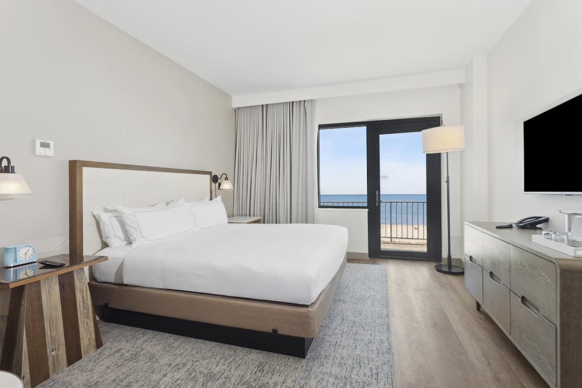 Habitació d'hotel moderna amb un llit gran, una taula de treball, una petarrera i una televisió. Té un balcó amb vistes al mar.