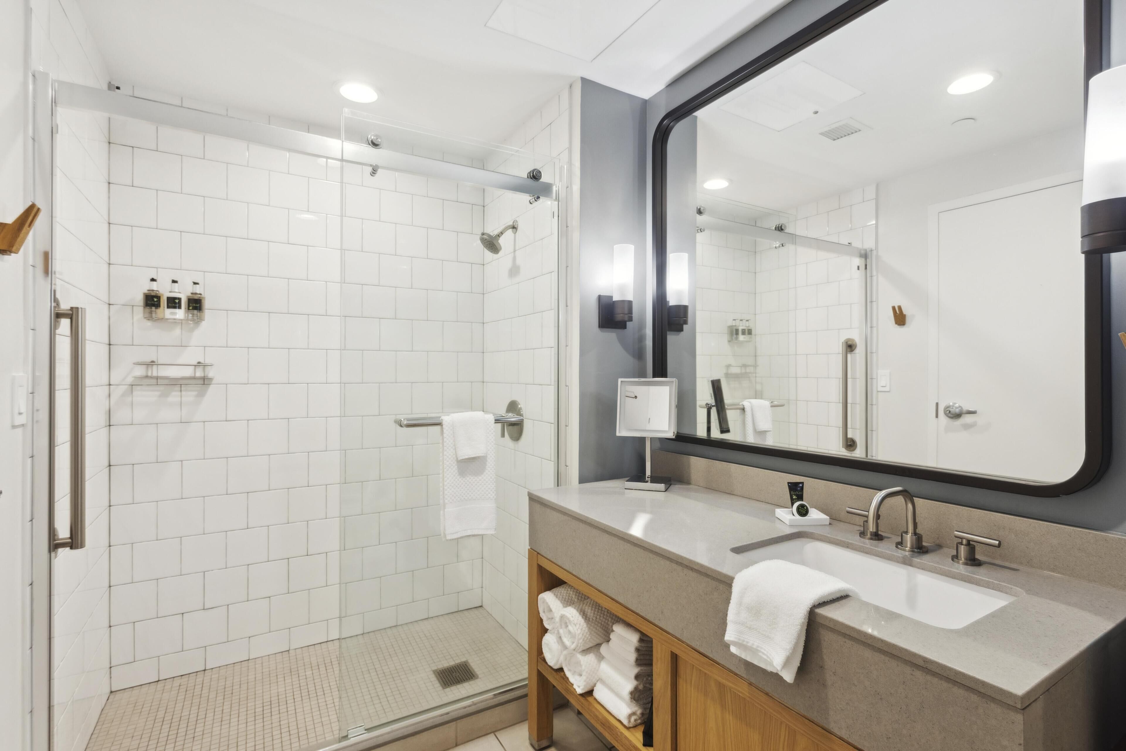 Une salle de bain moderne dotée d’une douche à l’italienne, d’un grand miroir et d’un meuble-lavabo avec un évier et un porte-serviettes.