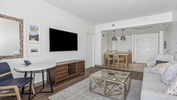A modern living room with a flat-screen TV, a dining area with a table and chairs, and a sofa.