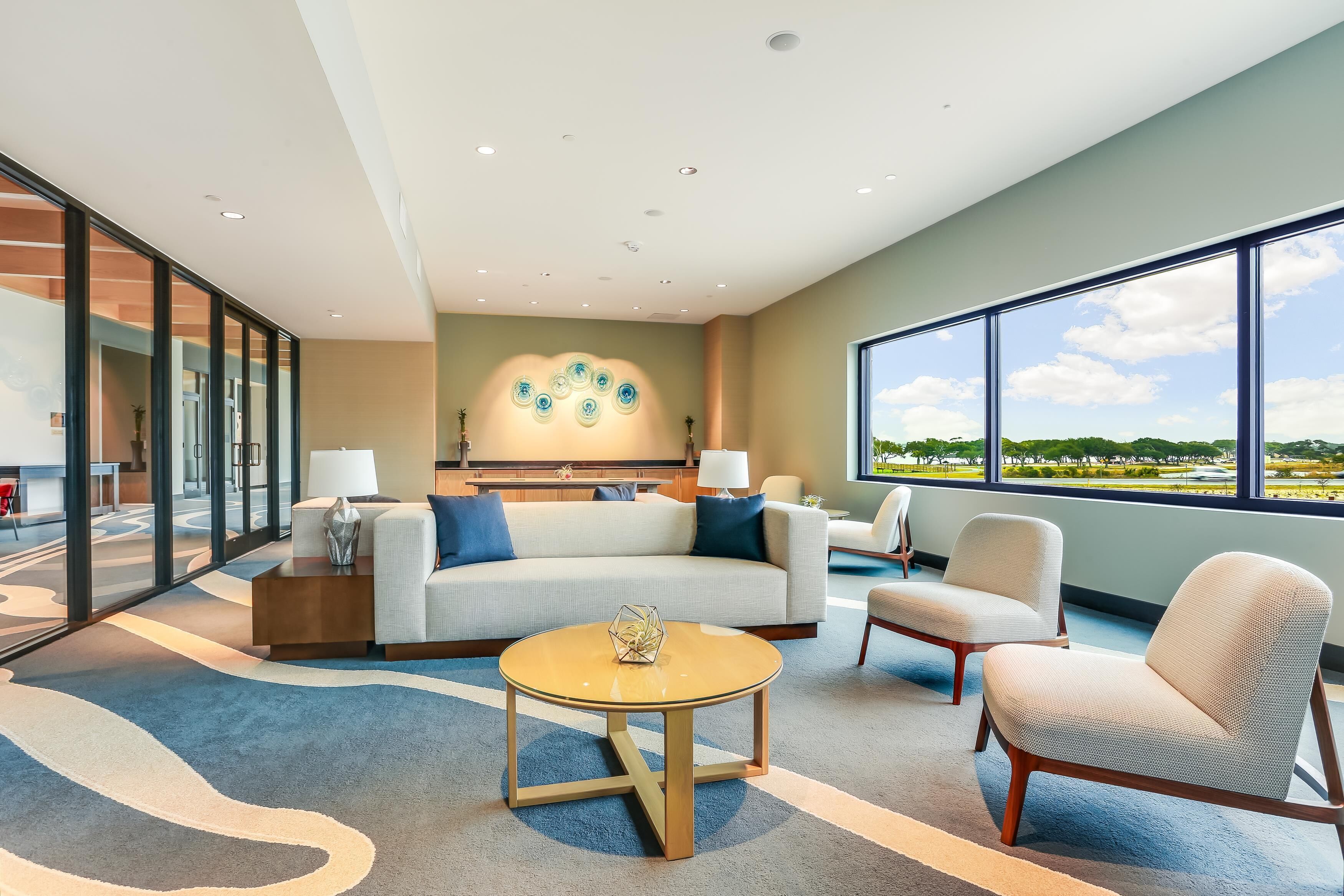 A modern hotel room with a large window, a sofa, a coffee table, and a chair.