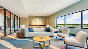 A modern hotel room with a large window, a sofa, a coffee table, and a chair.