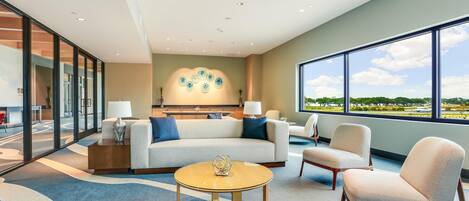 A modern hotel room with a large window, a sofa, a coffee table, and a chair.