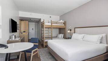 A hotel room with a bunk bed, a desk with a chair, a TV, and a small kitchenette.