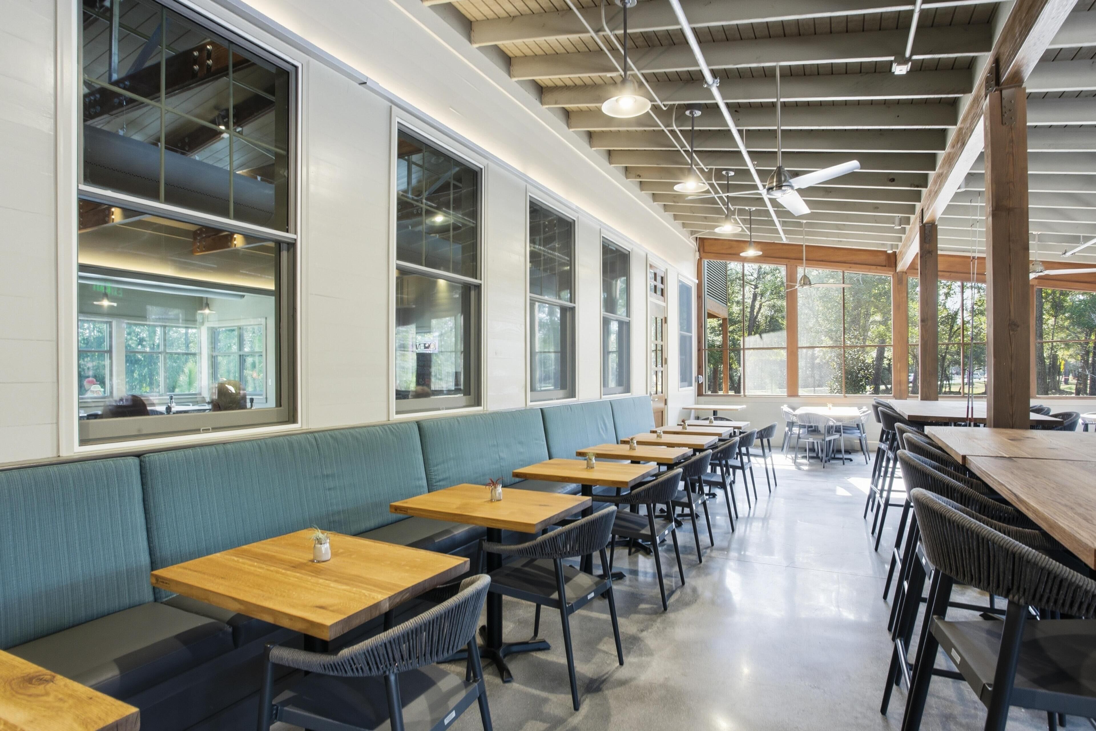 A modern restaurant interior with high ceilings, large windows, and a mix of seating options including booths and tables.