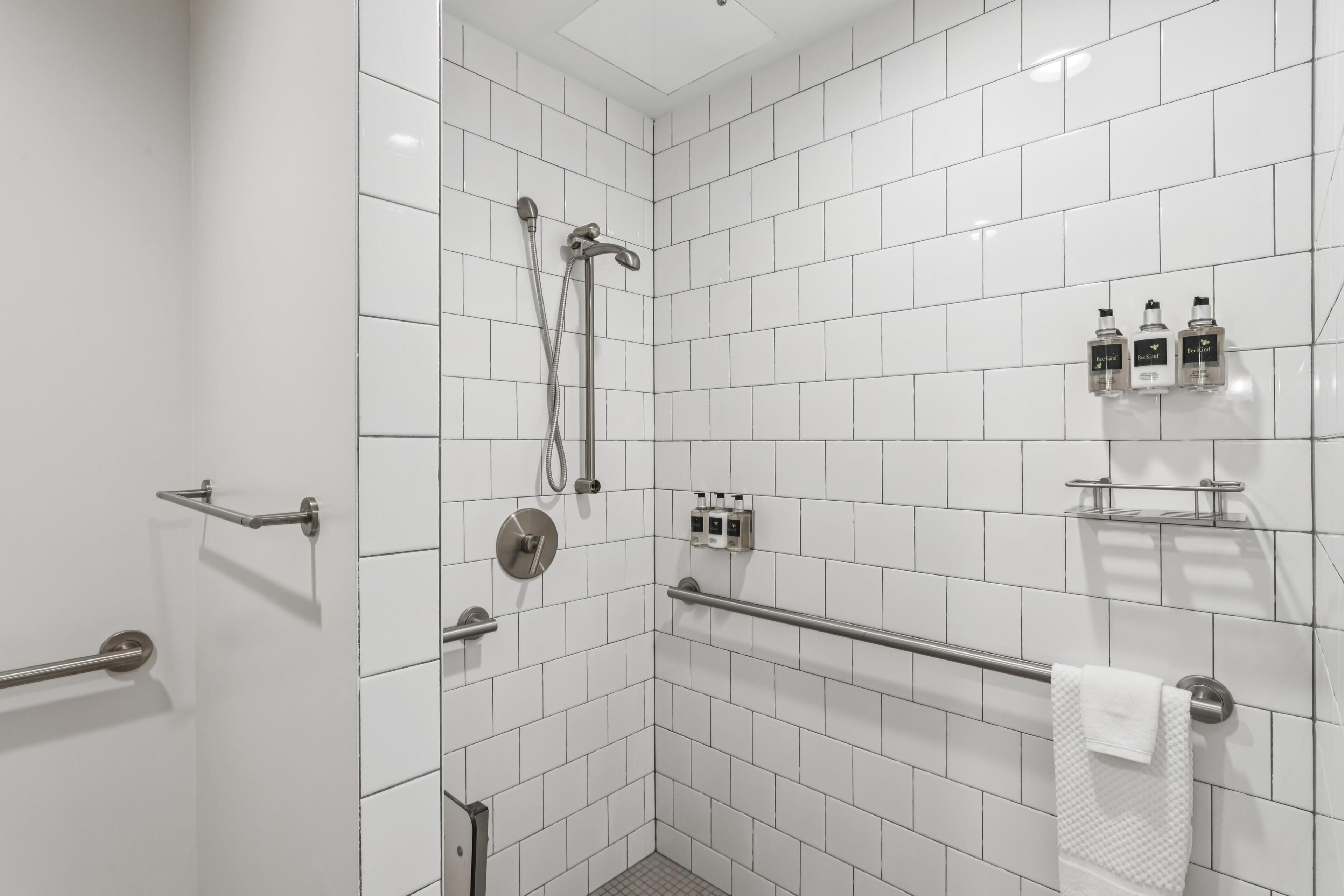 A modern bathroom with white tiles, a shower, a handrail, and a towel rack.