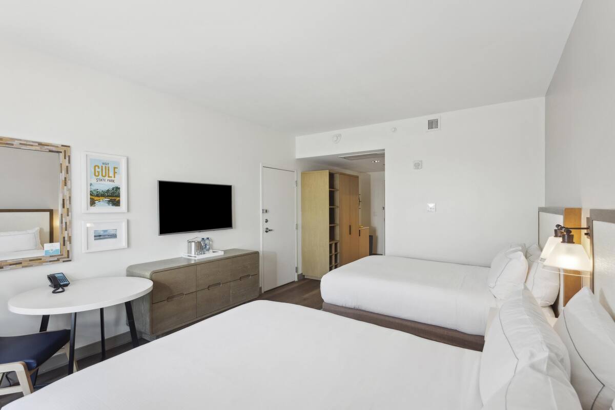 Habitació d'hotel amb dos llits, una televisió, un escriptori i una taula petita.