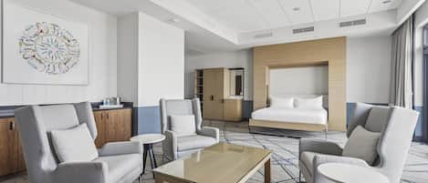 A hotel room with a large bed, two armchairs, a coffee table, a desk, and a wall-mounted TV.