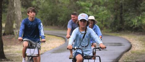 Un groupe de personnes fait du vélo sur un chemin pavé, entouré d’arbres.