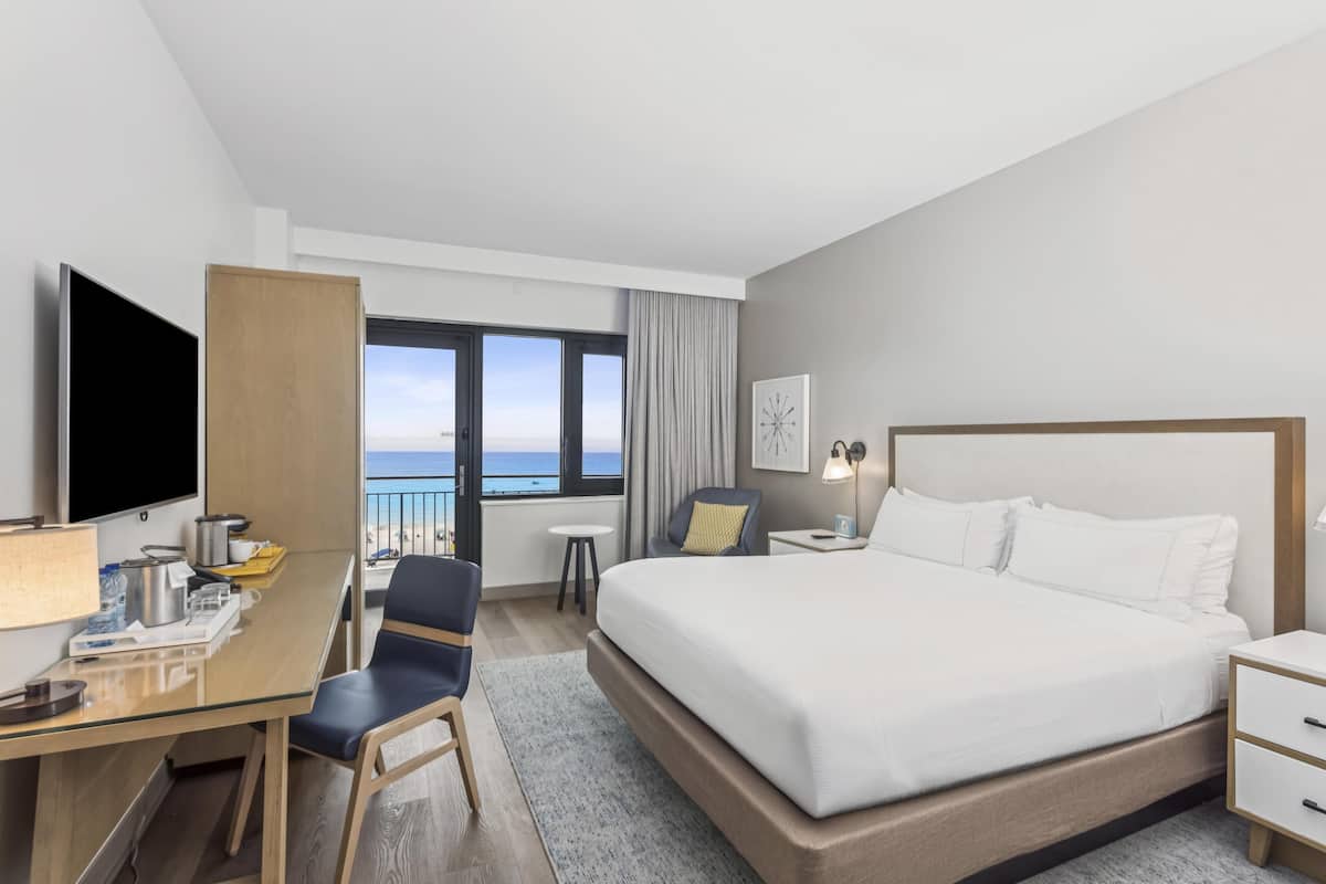 Habitació d'hotel amb un llit gran, una escriptori amb un ordinador, una cadira, un televisor i vista a l'oceà.