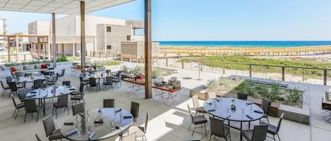 An outdoor dining area with tables and chairs, overlooking a beach.