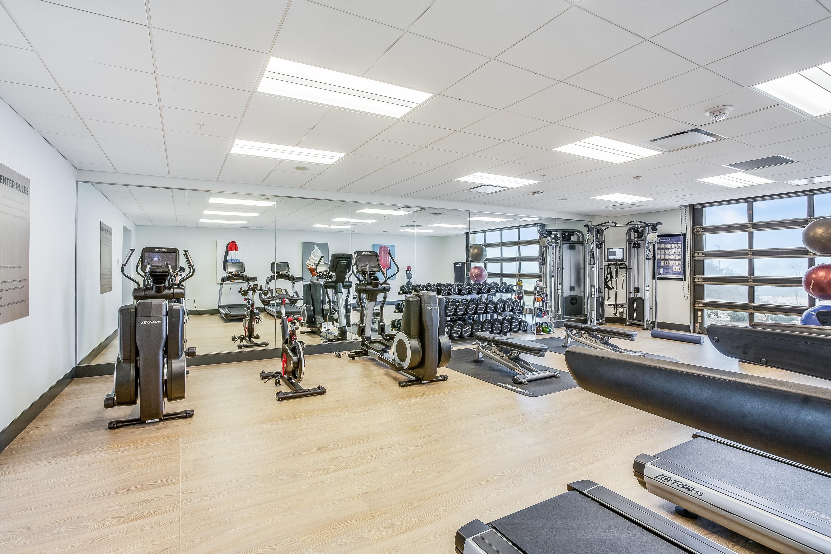 A gym with cardio machines, weightlifting equipment, and a mirrored wall.