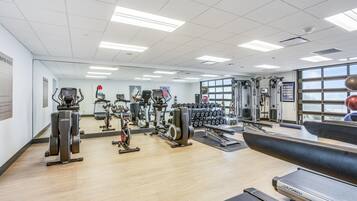 A gym with cardio machines, weightlifting equipment, and a mirrored wall.