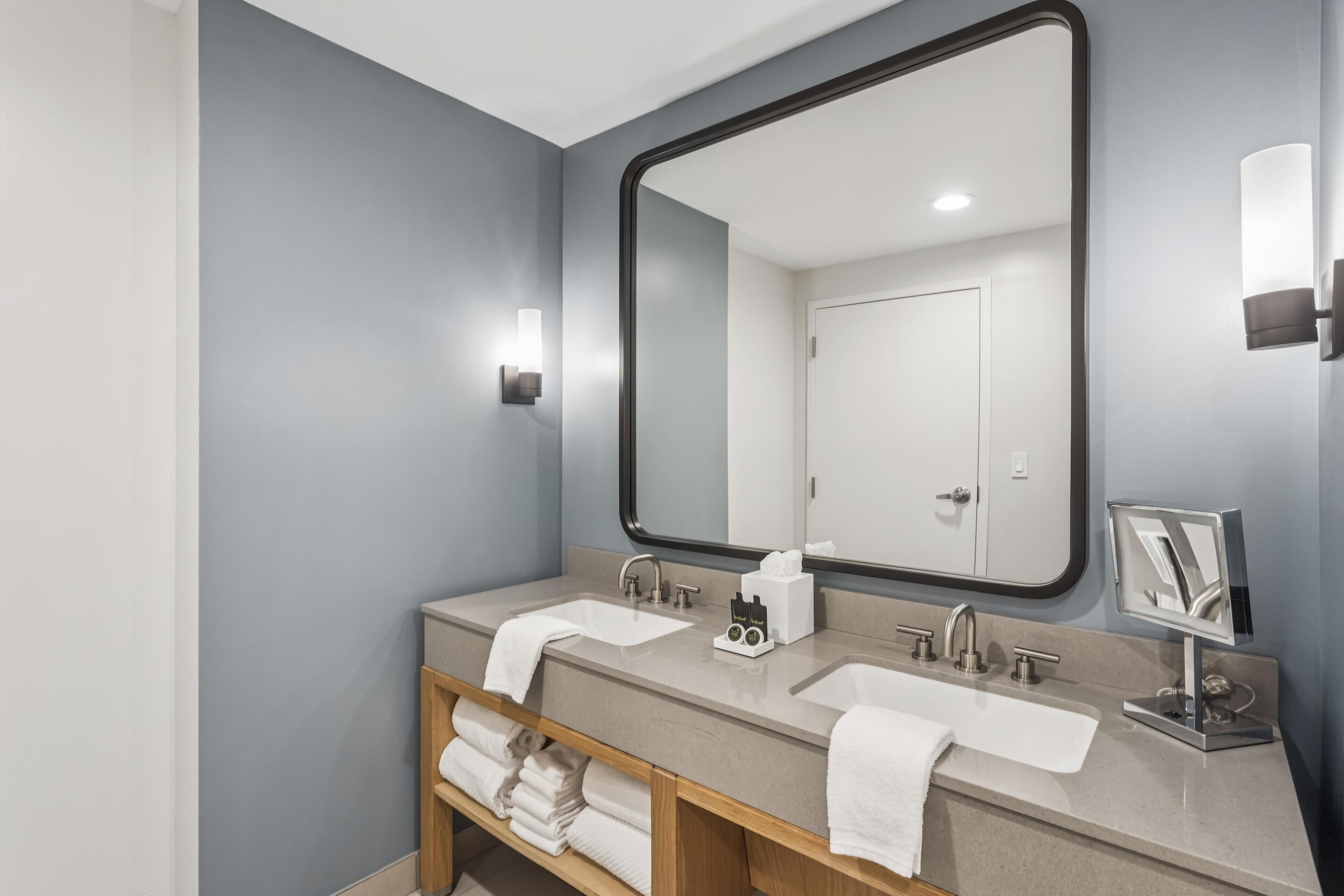 Een moderne badkamer met twee wastafels, een grote spiegel en een handdoekhouder.