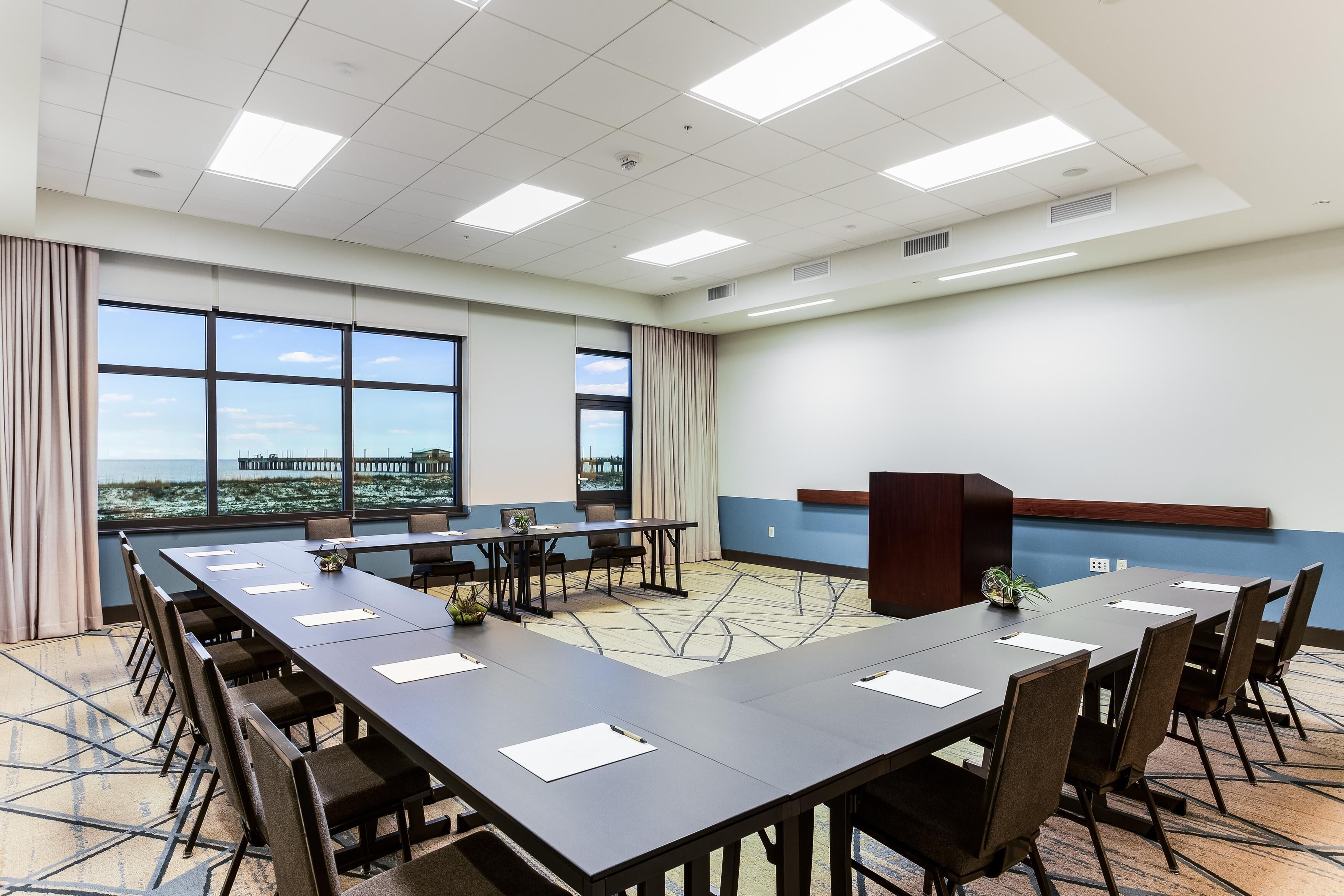 A conference room with a long table, chairs, a podium, and large windows with a view.