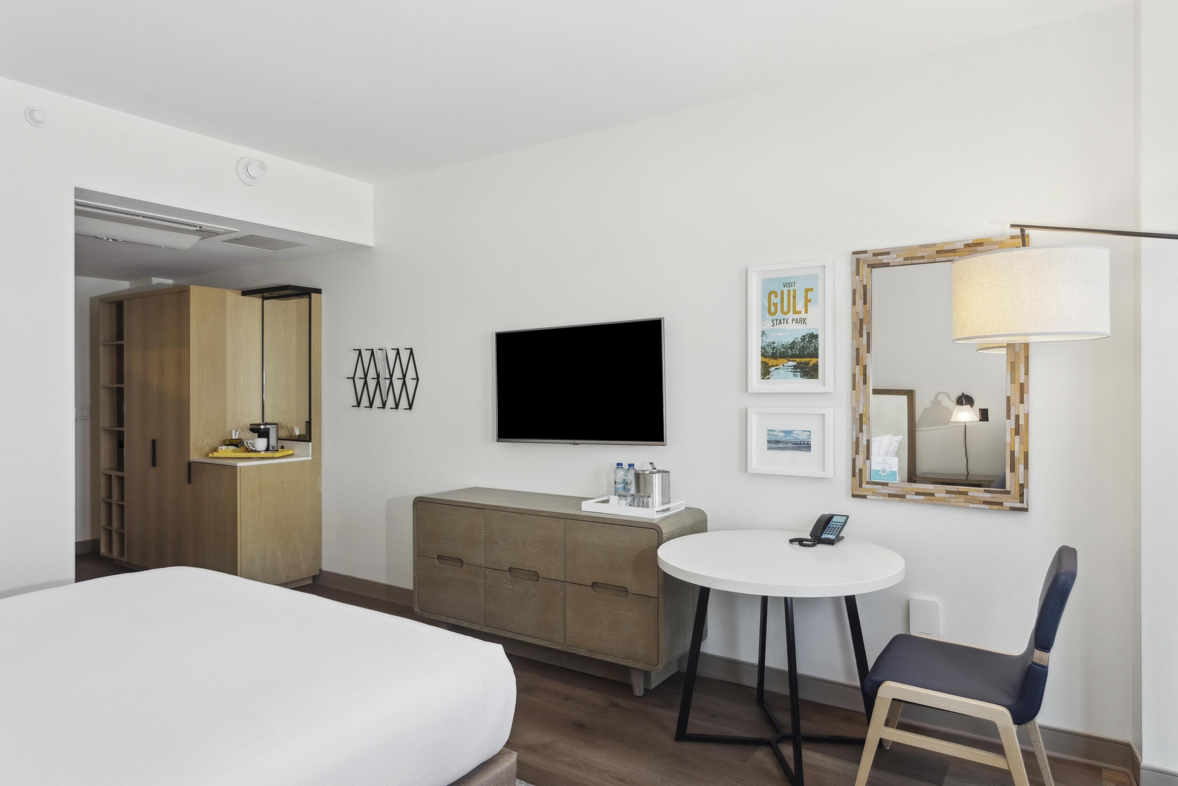 A hotel room with a bed, a desk, a chair, a TV, a minibar, and a wardrobe.