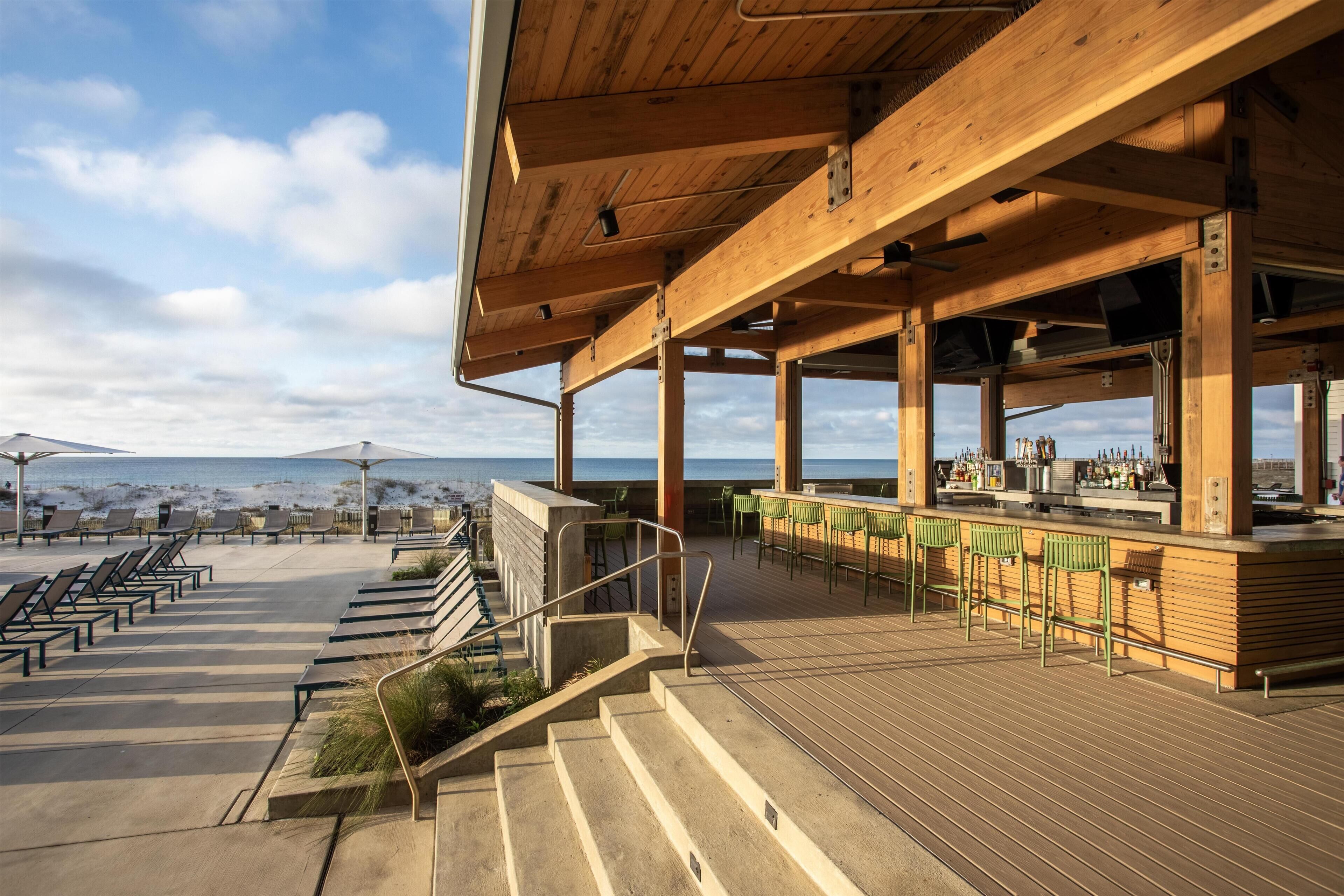 A wooden deck with outdoor seating, a bar area, and a view of the ocean.