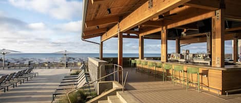 A wooden deck with outdoor seating, a bar area, and a view of the ocean.