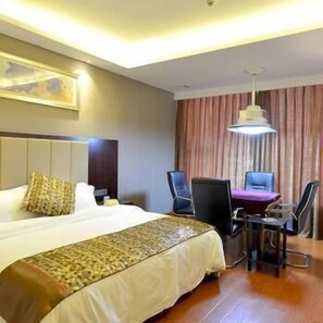 Een hotelkamer met een groot bed, een bureau met twee stoelen, een bureaulamp en een schilderij aan de muur.