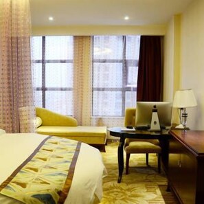 Een hotelkamer met een groot bed, een bureau met lamp, een stoel en een raam met gordijnen.