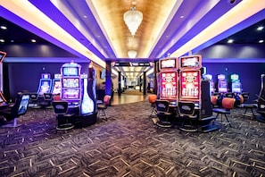 Un casino doté de nombreux appareils à sous et de tables de jeux, d’un tapis à motifs et d’un lustre.