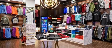 A clothing store with racks of colorful apparel, a display table with folded clothes, and a Pepsi refrigerator.