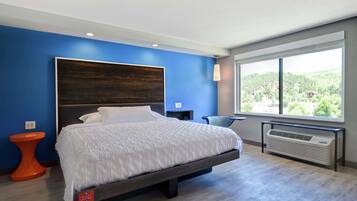 A modern hotel room with a large bed, a view of greenery, and a built-in air conditioning unit.