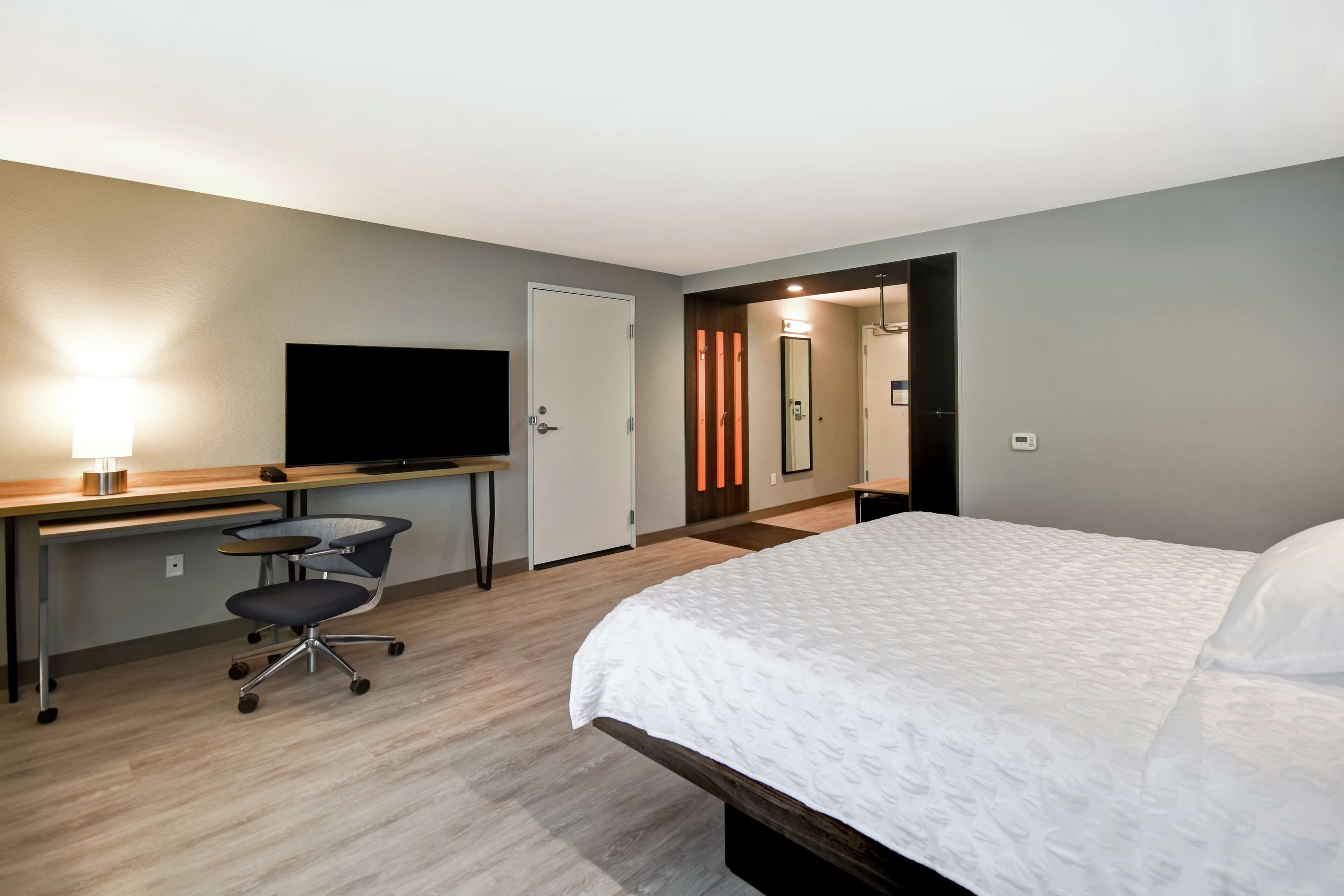 A hotel room with a bed, desk, chair, TV, and a mirror.