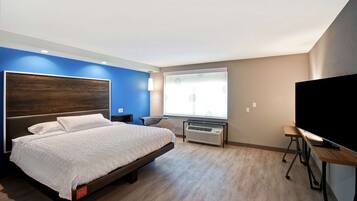 A modern hotel room with a large bed, a flat-screen TV, a desk, and a window with blinds.