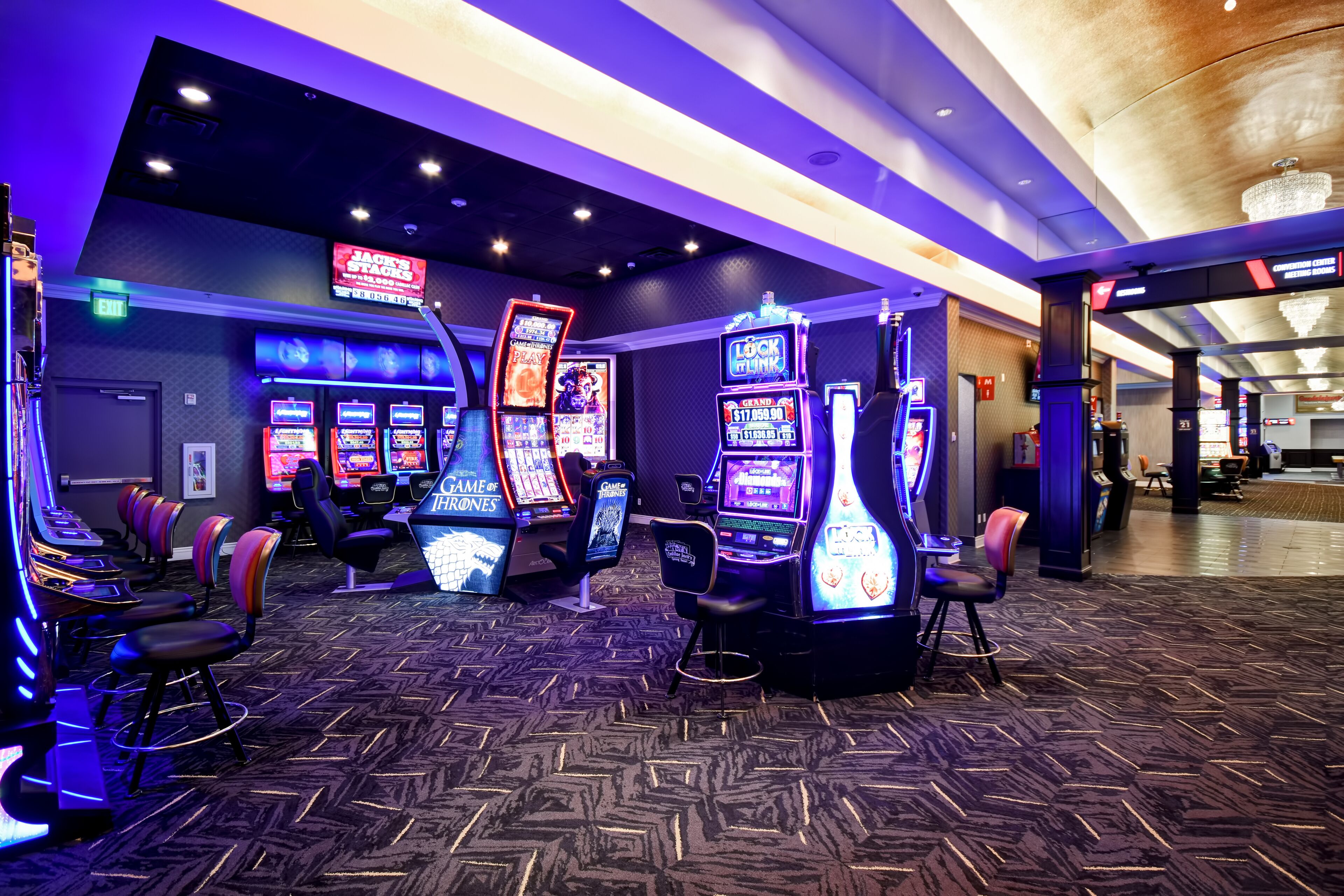 A casino area with slot machines, gaming chairs, and a neon sign advertising 'Jack's Stacks'.