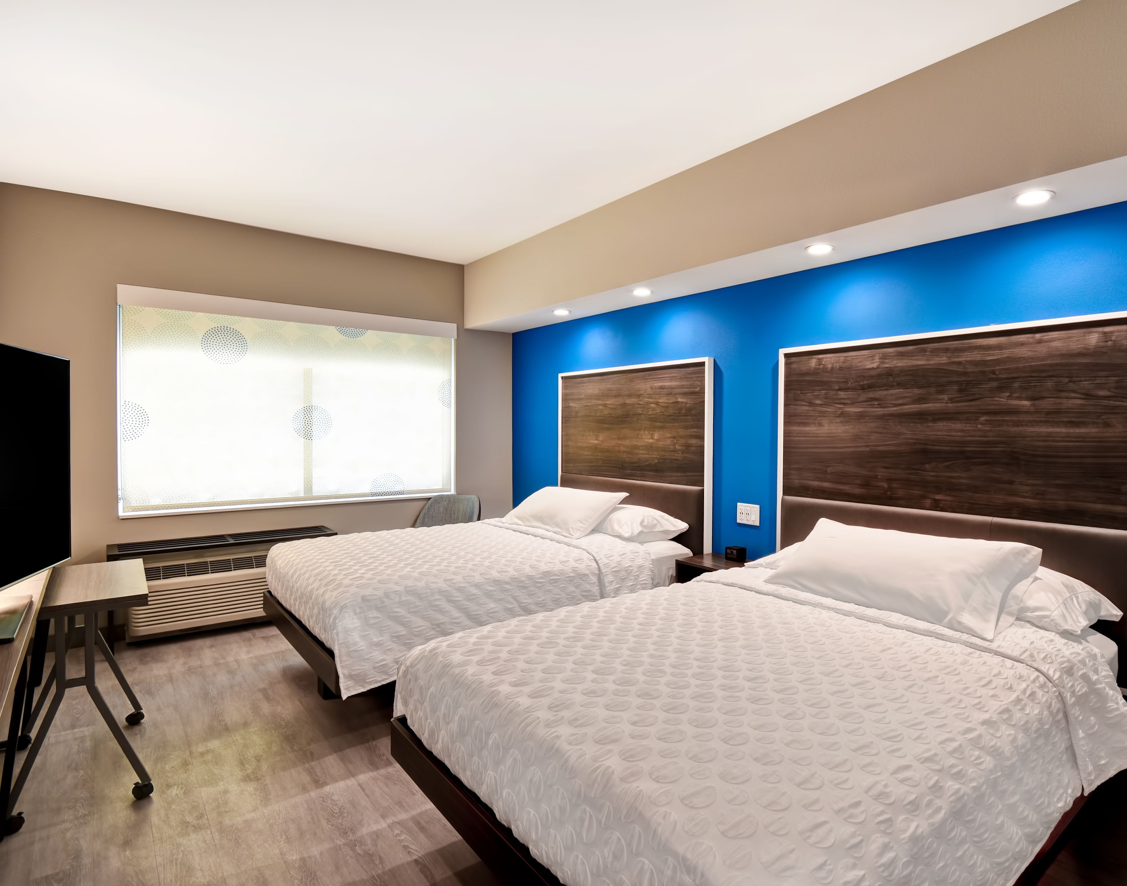 Une chambre d’hôtel avec deux lits, un bureau et une grande fenêtre avec des stores.