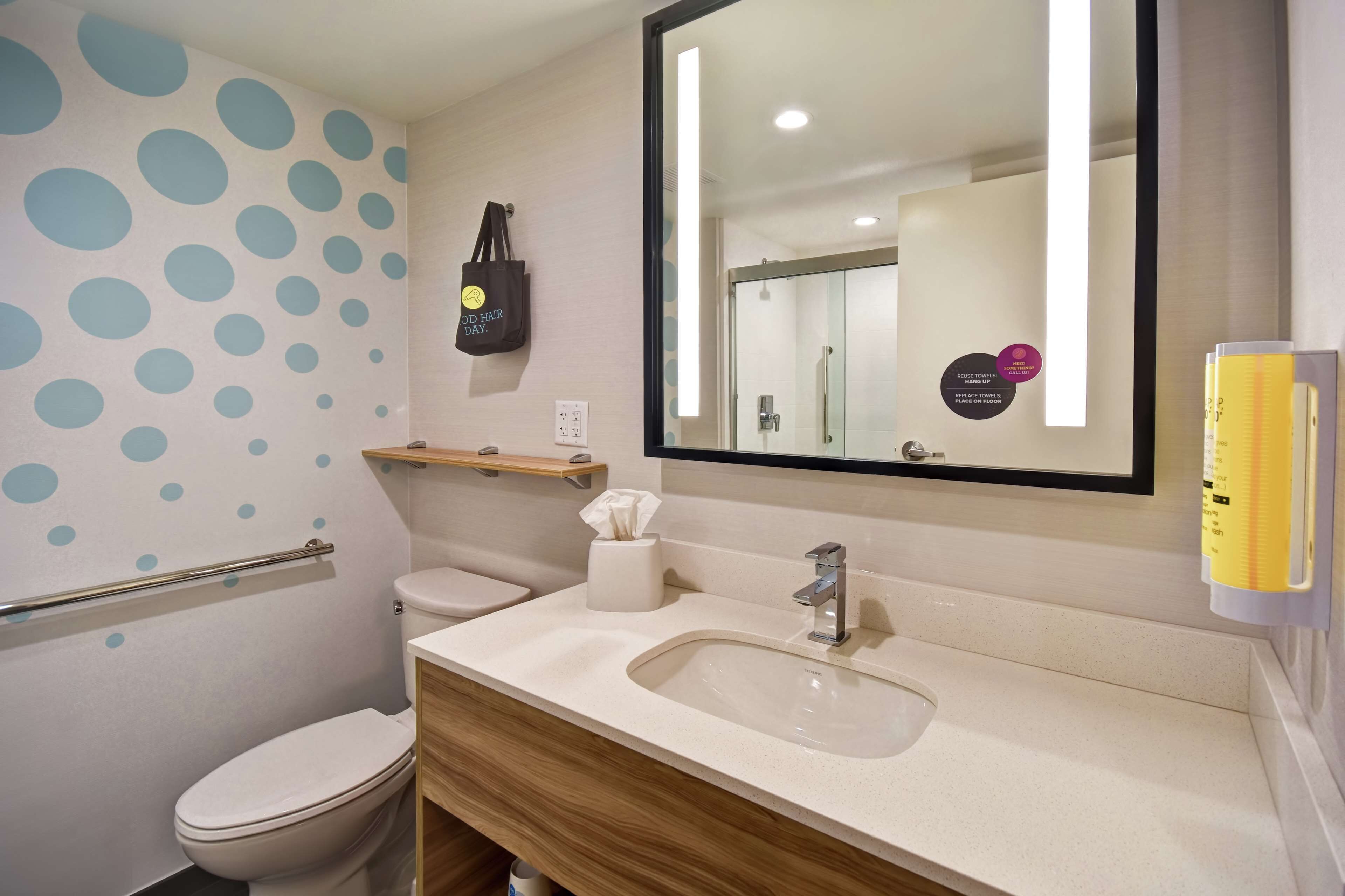 A bathroom with a toilet, sink, mirror, and a wall with blue polka dots.